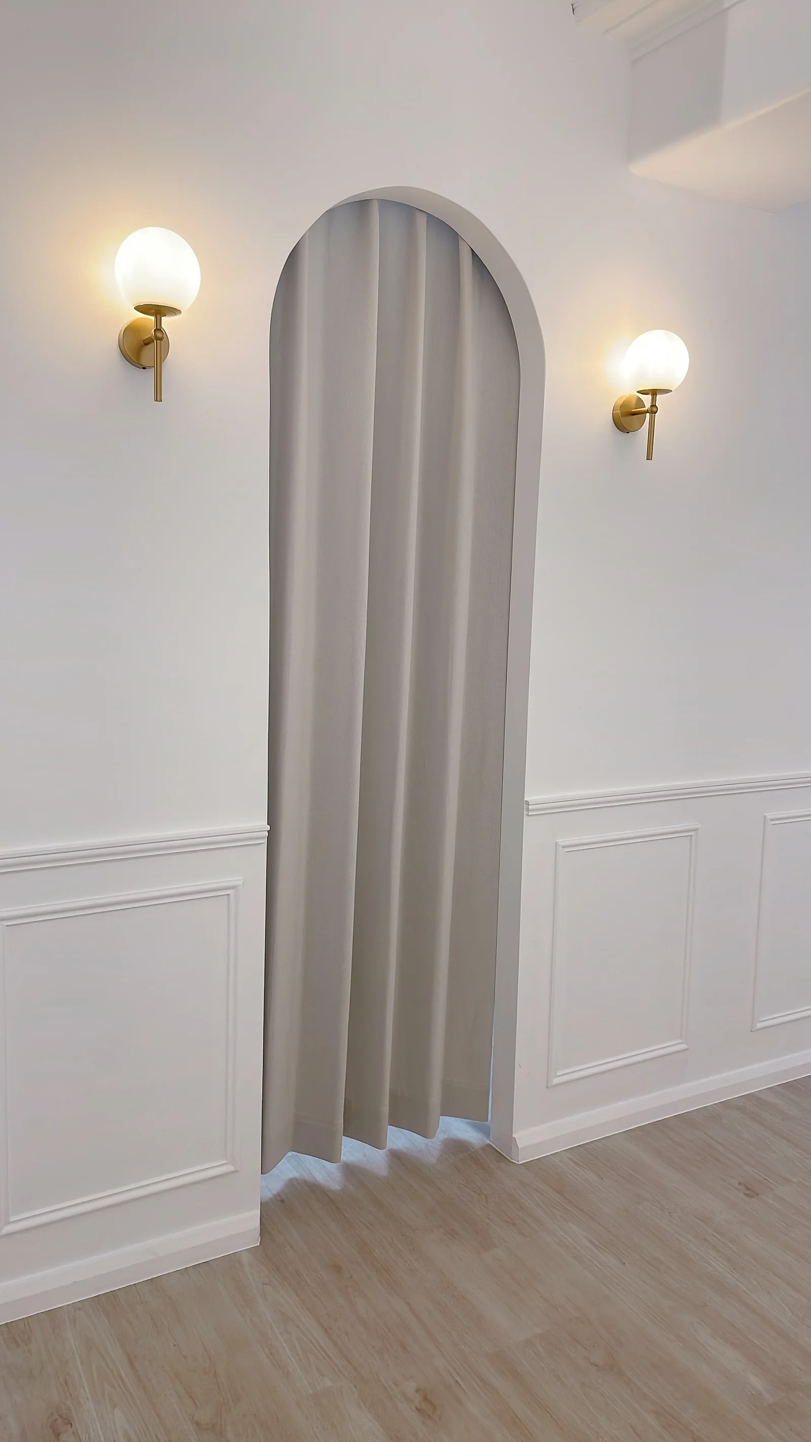 Arched doorway with curtain and gold globe sconces inside éclaire beauty studio